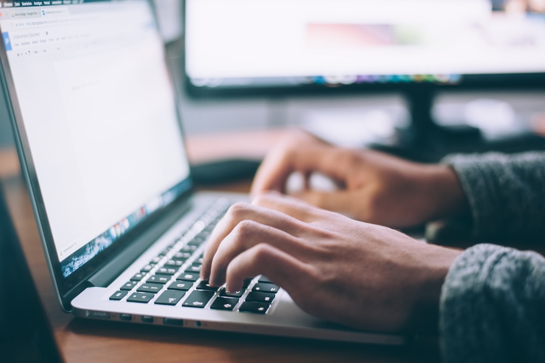 Lähivõte inimese kätest, kes trükib sülearvuti klaviatuuril, taustal on laual teine arvutimonitor—ideaalne WordPressi hostimisülesannete haldamiseks.